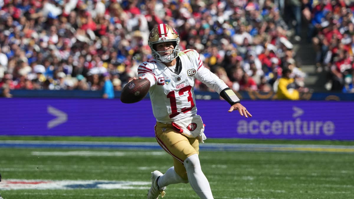 Brock Purdy in a white 49ers jersey with red and gold trim, number 13, throws a football on the field.
