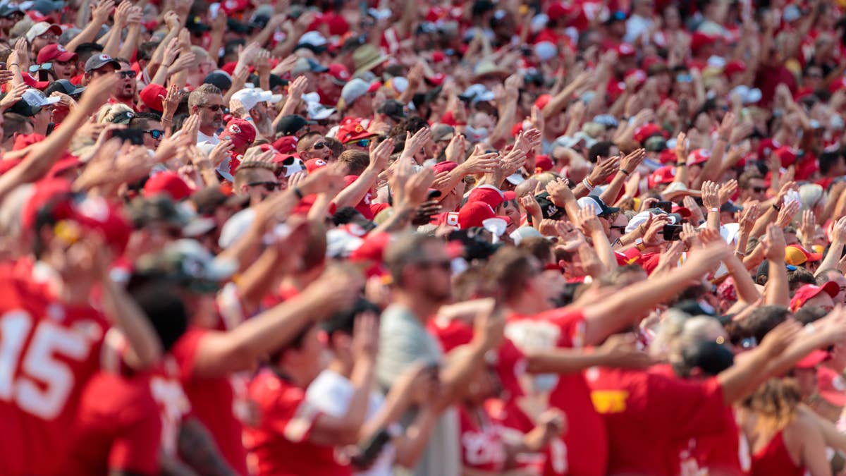 Kansas City Chiefs fans in red jerseys, one with number 15, cheer with hands raised.