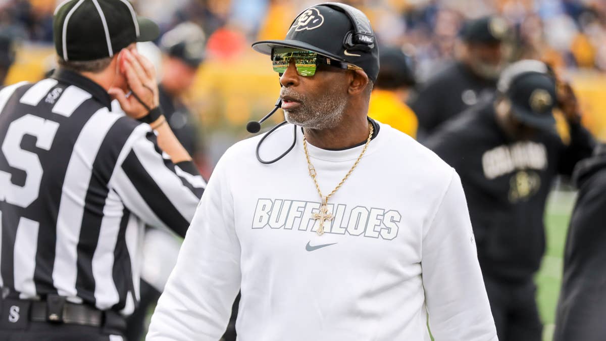 Coach Prime wearing a white sweatshirt with "BUFFALOES" across it, a black Colorado hat, and sunglasses.