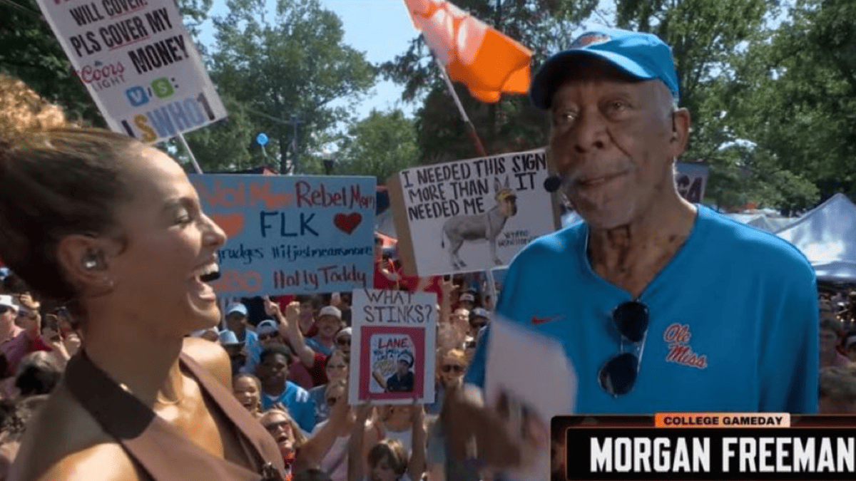 Morgan Freeman in a blue Ole Miss shirt and cap speaks to a woman at College GameDay.