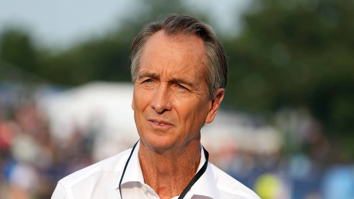 Cris Collinsworth in a white collared shirt with a black lanyard, looking to the side.