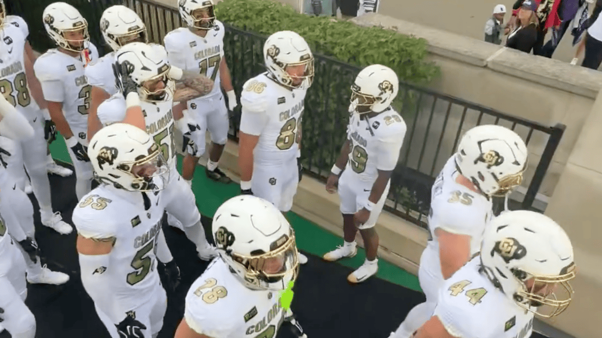 Colorado football players in white and gold uniforms walk together.