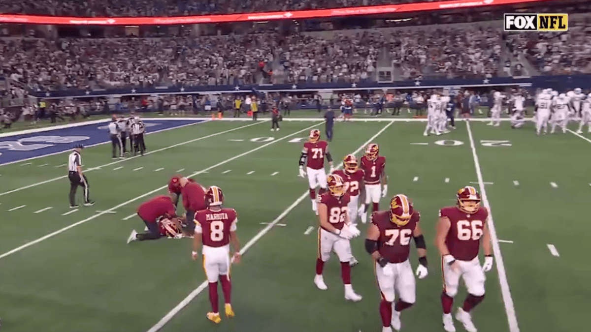 Washington Commanders players in burgundy and gold uniforms walk past a player on the ground, one with jersey number 8.