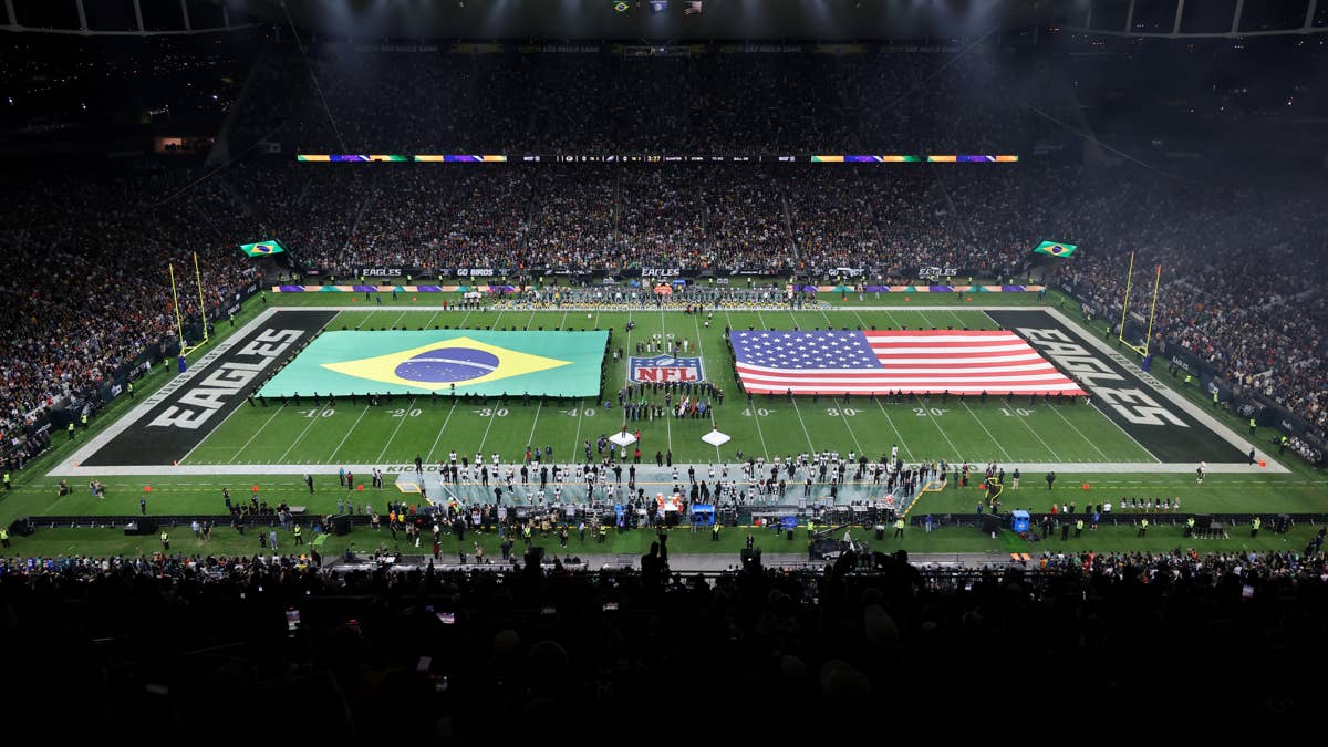 NFL game at Maracanã Stadium with players holding large Brazilian and US flags on the field.