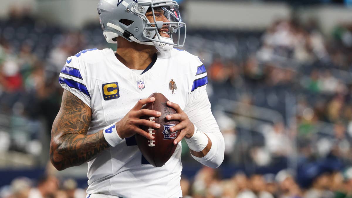 Dak Prescott in a white Cowboys jersey with blue trim and a C patch, holding a football.