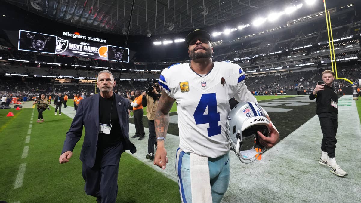 Dak Prescott in a white #4 Cowboys jersey walks off the field holding his helmet at Allegiant Stadium.