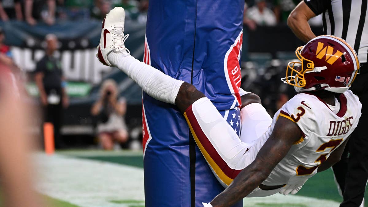 Stefon Diggs in a white Commanders jersey with burgundy and gold trim, number 13, leans against a goalpost.