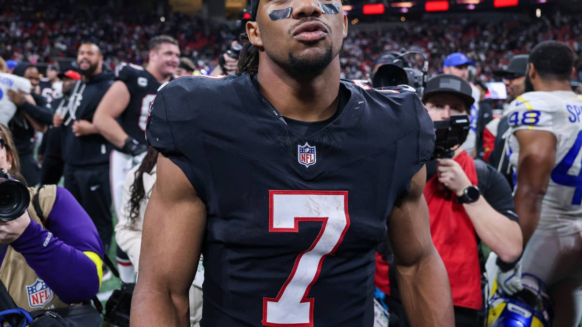 Bijan Robinson in a black Falcons jersey with number 7, surrounded by other players and media.