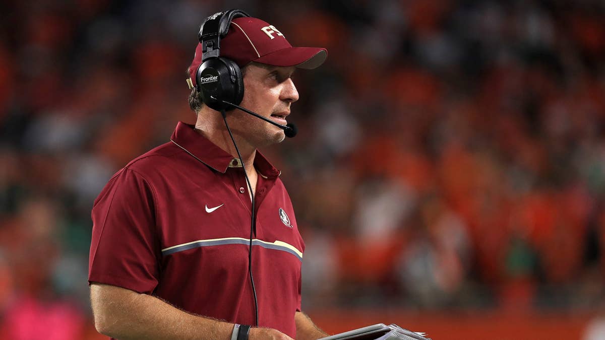 Jimbo Fisher in a maroon Florida State polo shirt and cap with headphones on, with a blurred crowd in the background.