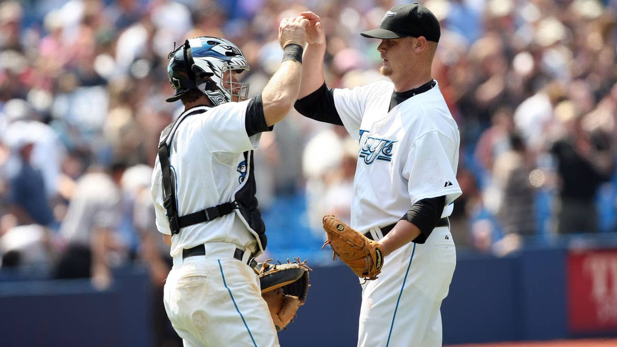 Brian Wolfe, wearing a Toronto Blue Jays uniform, high-fives a catcher in uniform.