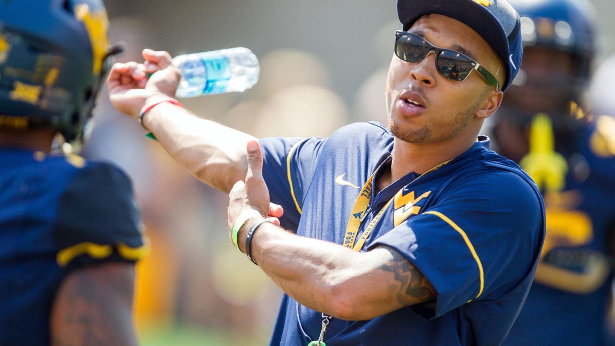 Stedman Bailey in a blue and yellow West Virginia shirt and baseball cap gestures with a water bottle.