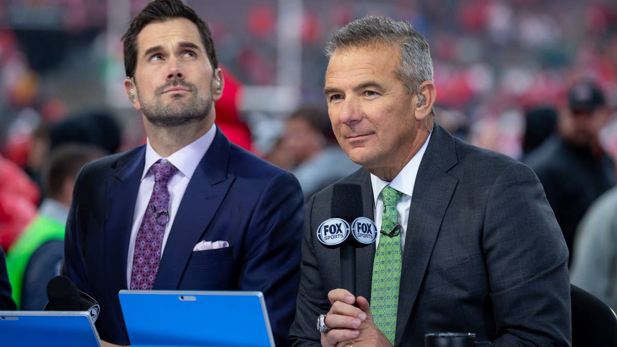 Urban Meyer and another man in suits with Fox Sports microphones at a football game.