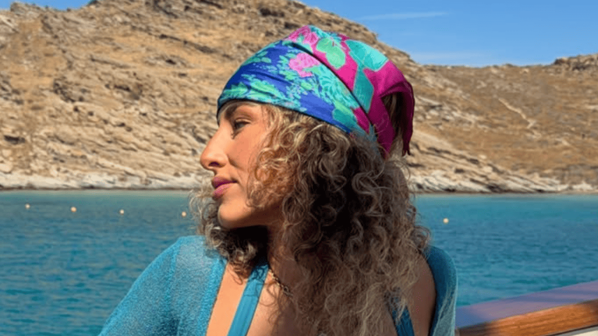 Gia Duddy in a blue swimsuit and colorful headscarf on a boat in Greece.