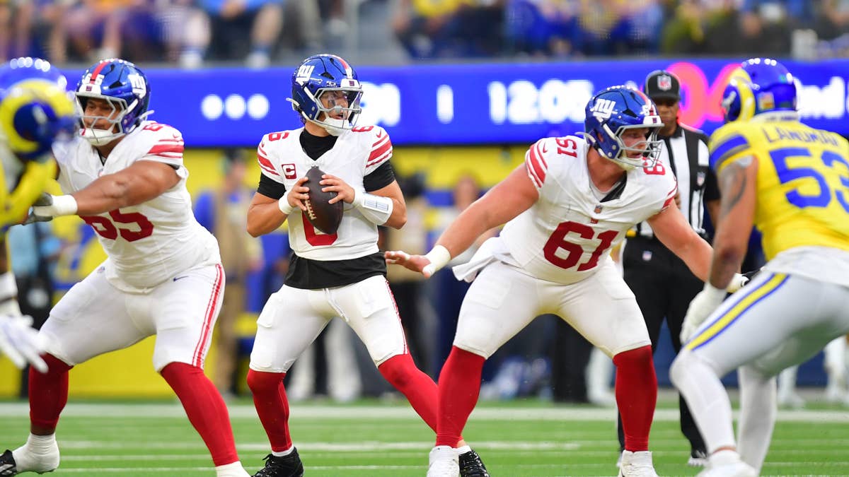 New York Giants quarterback Jaxson Dart (2) holds the ball while offensive linemen wear white jerseys with red trim and blue helmets.
