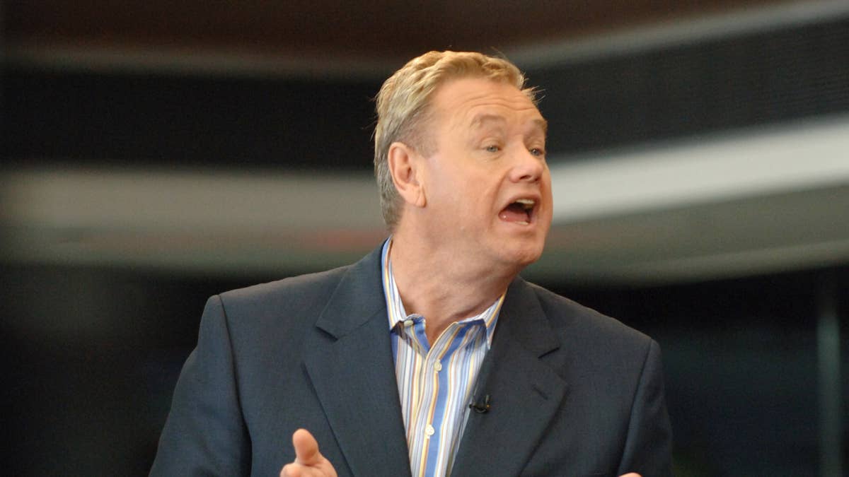 Woody Paige in a suit and striped shirt speaks animatedly.