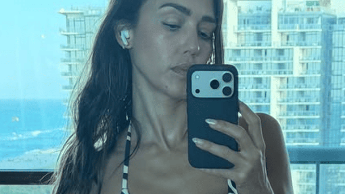 Jessica Alba takes a selfie in a black and white striped top, holding her phone in front of a city skyline.