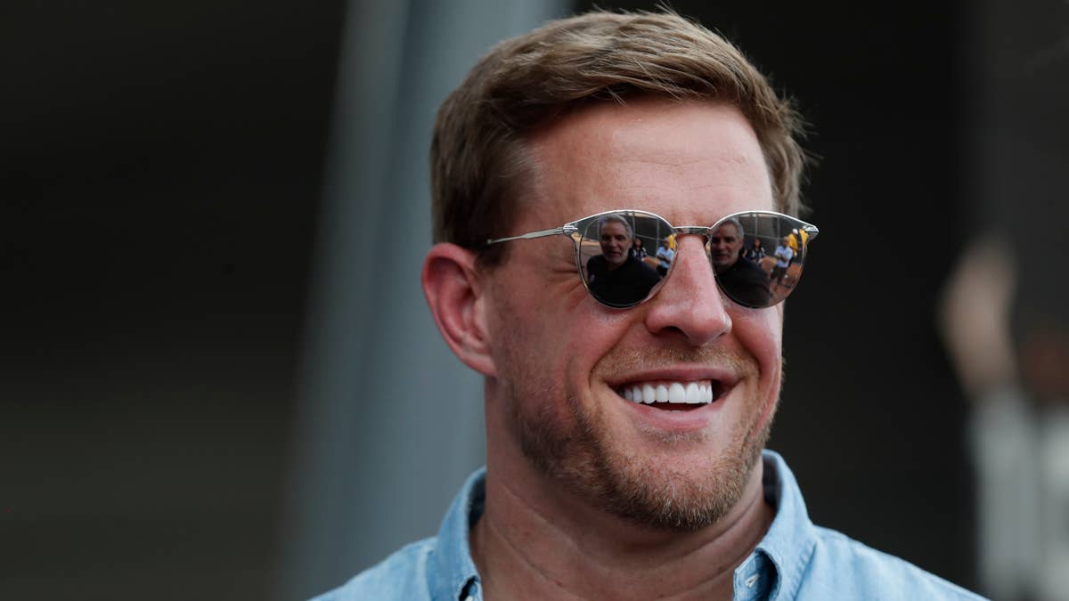 JJ Watt wearing sunglasses, with reflections of people in them, smiles in a light blue shirt.