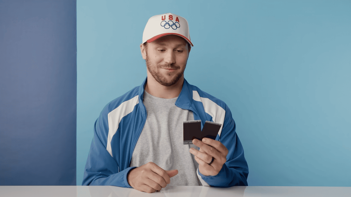 Josh Allen in a USA Olympic hat and blue jacket holds two Polaroids.