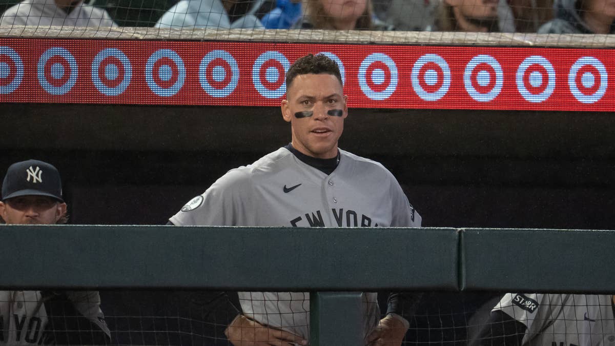 Aaron Judge in a gray New York Yankees uniform and black eye black, standing in a dugout.