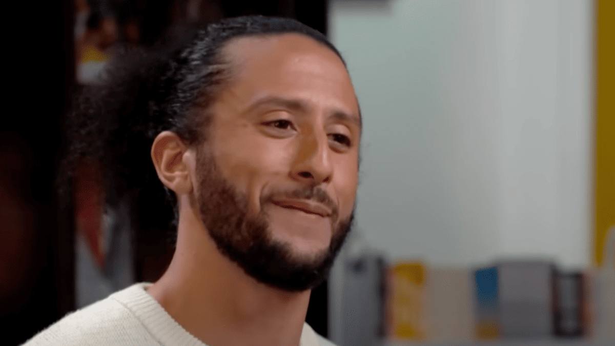 Colin Kaepernick smiles wearing a cream sweater.