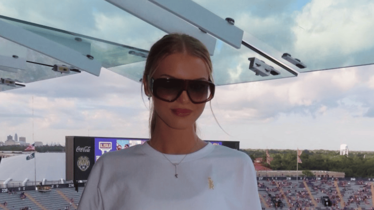 Landry Kiffin wears a white t-shirt and sunglasses at a football stadium with LSU logos.