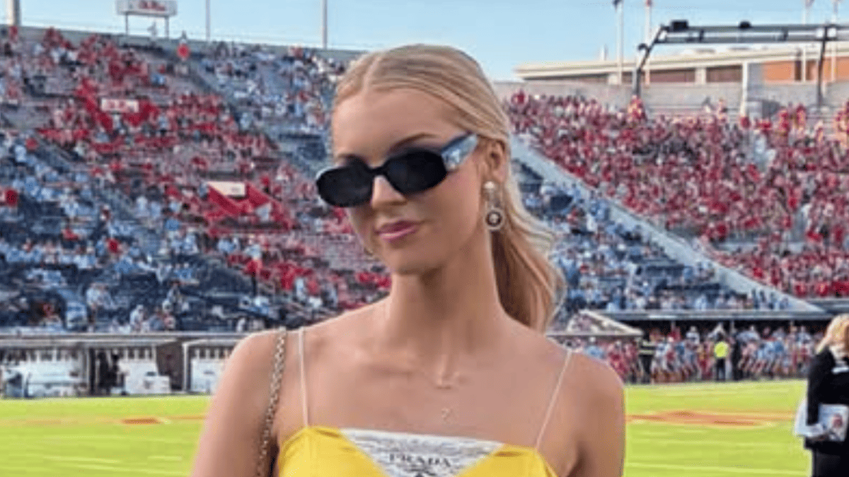 Landry Kiffin in yellow Prada dress and sunglasses at football game with red and blue seats.