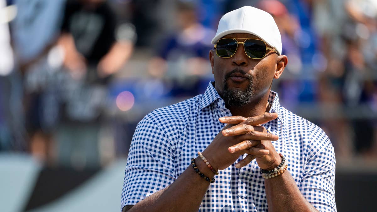 Ray Lewis wearing a white hat, sunglasses, and blue checkered shirt with hands clasped.
