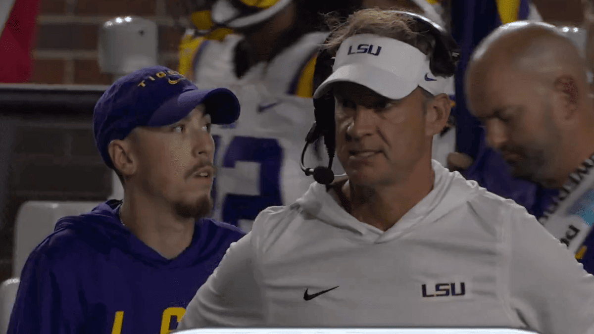 Lane Kiffin in white LSU hoodie and visor, with a young man in a purple LSU hoodie and hat.