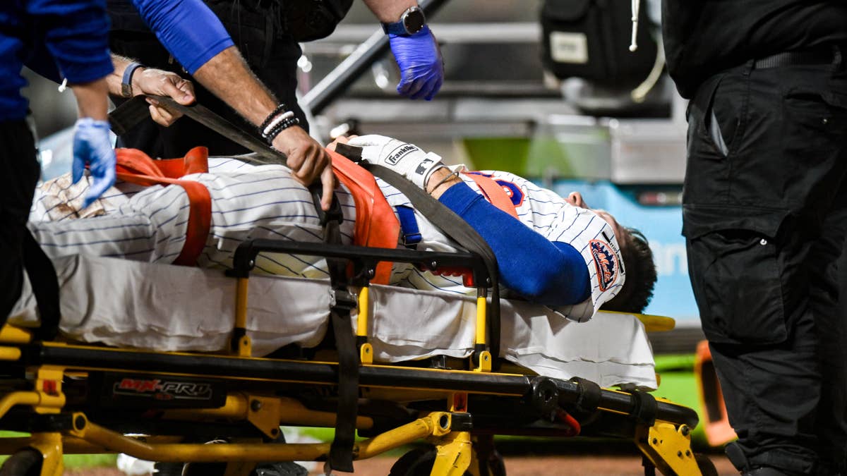 Jared Young in a Mets uniform on a stretcher, with medical personnel handling him.