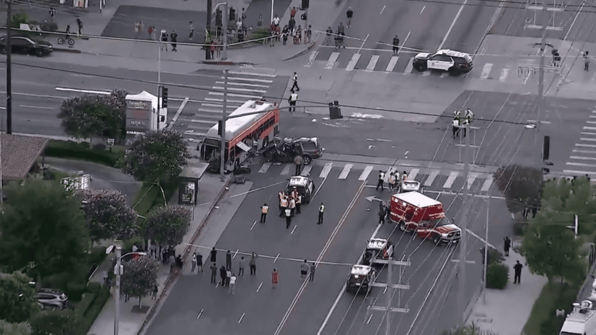 Aerial view of a bus and car crash at an intersection with emergency vehicles and onlookers.