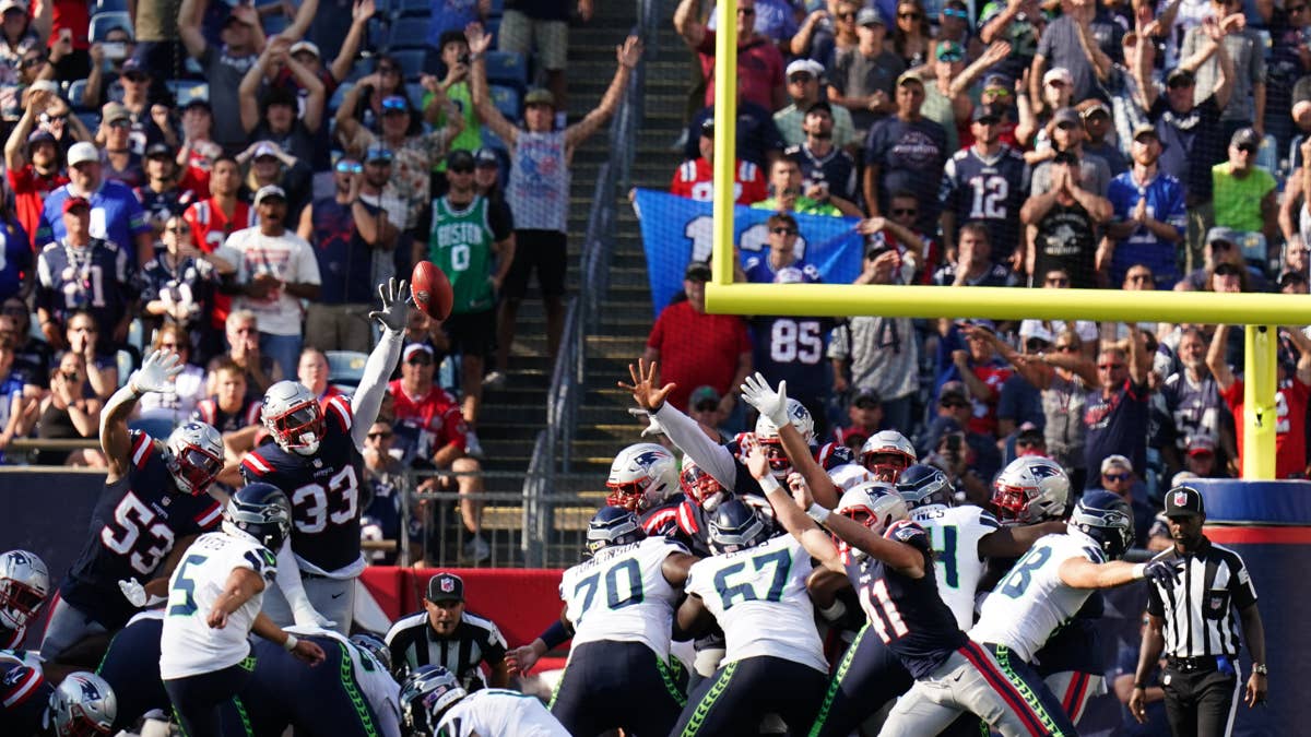 New England Patriots players in white and navy uniforms attempt to block a field goal as a football flies through the air.