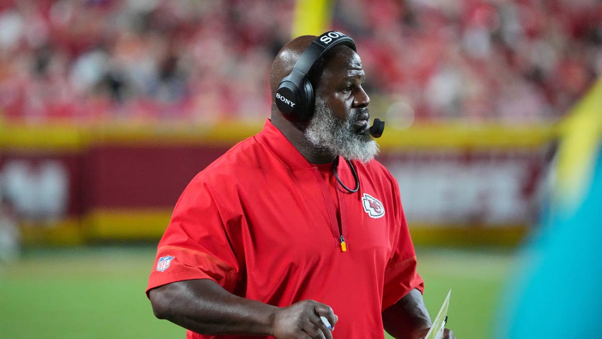 Eric Bieniemy in a red Kansas City Chiefs jacket and Sony headphones on the sideline.