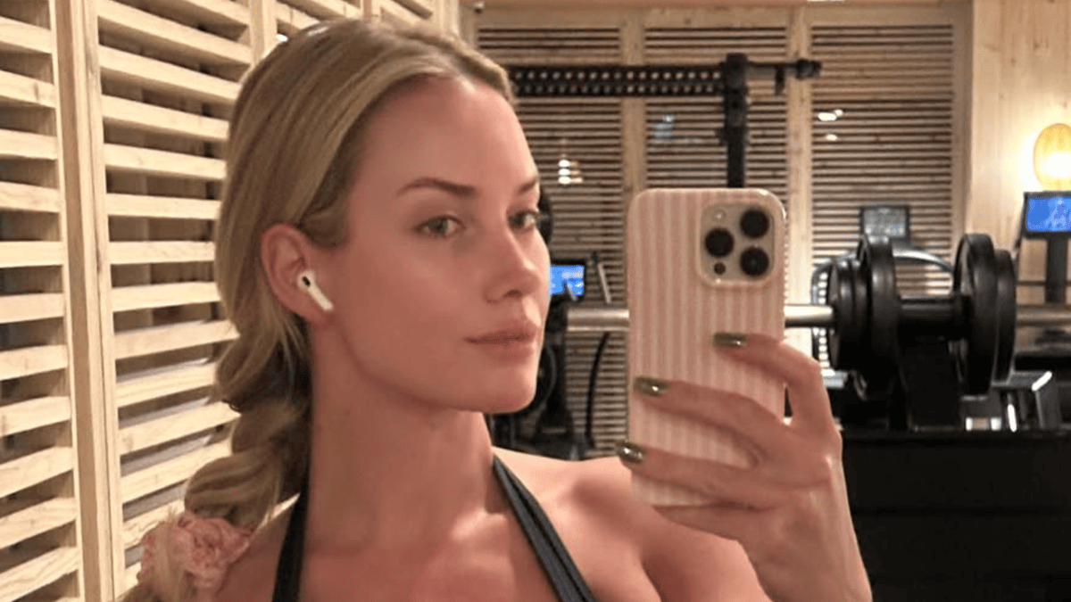 Paige Spiranac in a gym wearing a sports bra, taking a selfie with a phone.