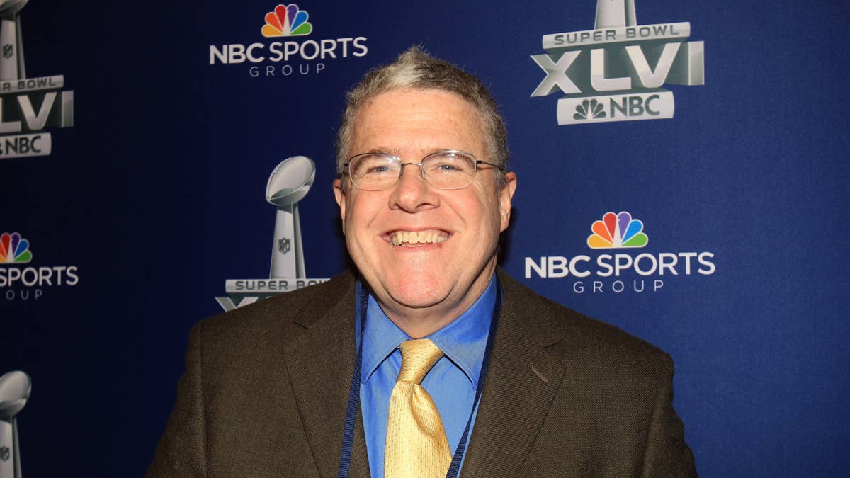 Peter King smiles in front of a Super Bowl XLVI NBC Sports backdrop with Lombardi trophies.