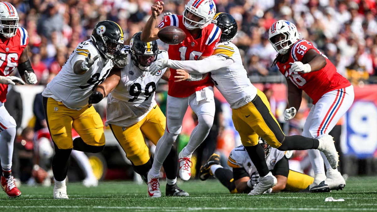 Patriots quarterback in red jersey #10 is tackled by Steelers players in white and yellow uniforms.