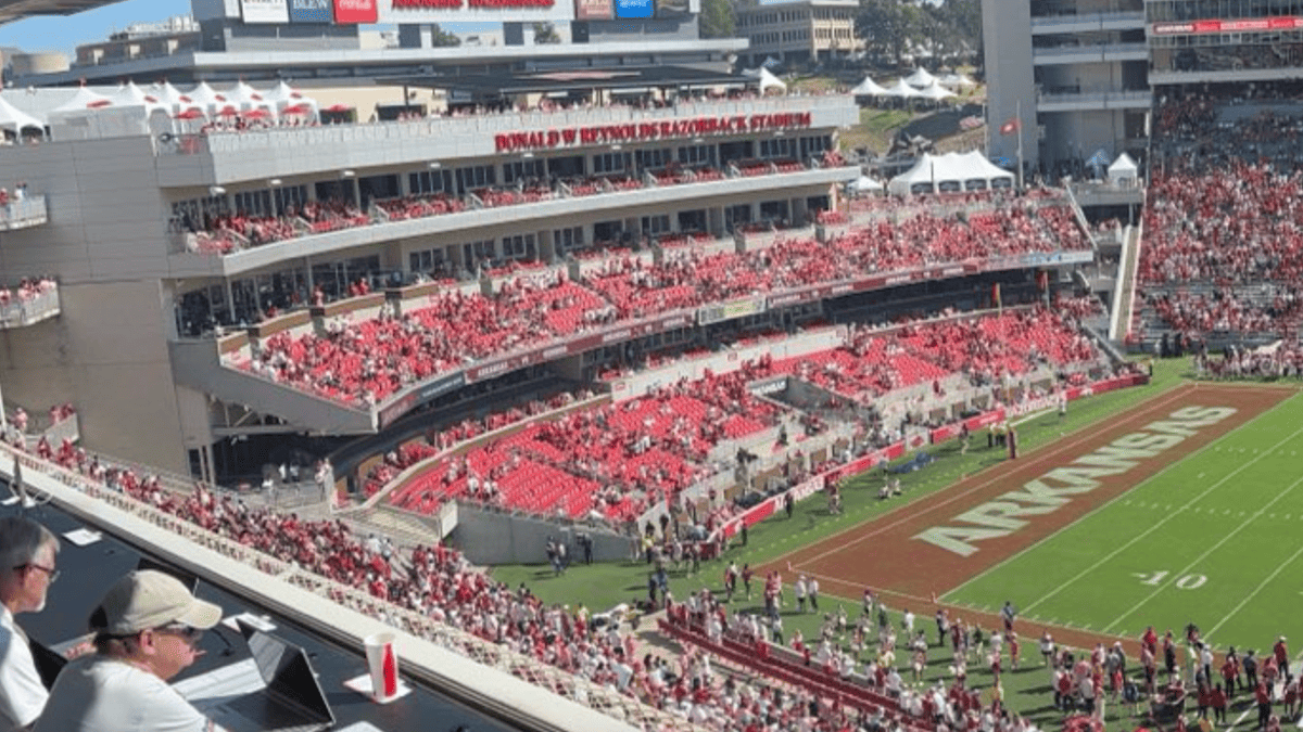Empty red seats in Donald W. Reynolds Razorback Stadium with "ARKANSAS" on the field.