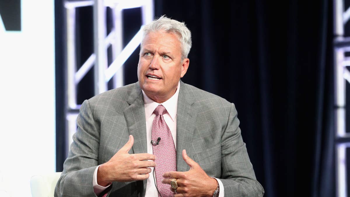Rex Ryan in a grey suit and pink tie speaks with his hands gesturing.