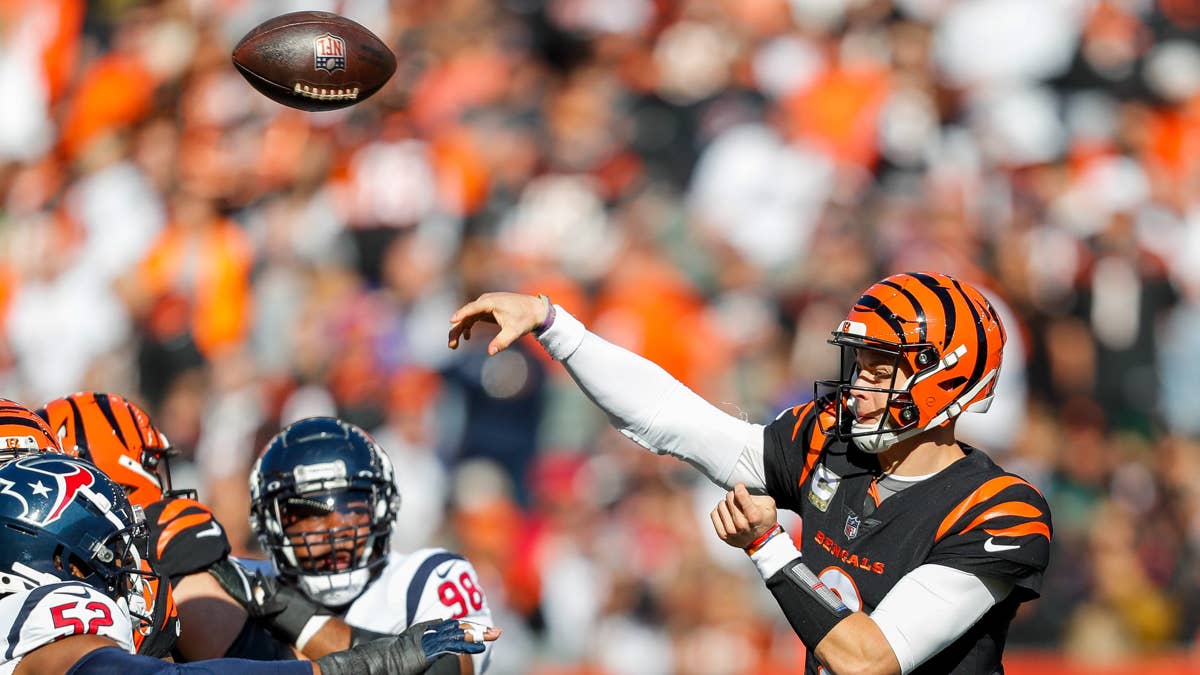 Joe Burrow in a black and orange Bengals uniform throws a football during a game.