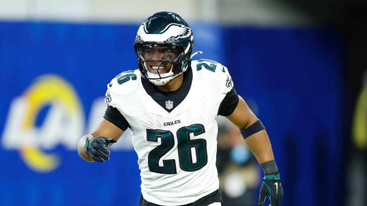Saquon Barkley in Eagles #26 jersey on field with blurred Rams logo in background