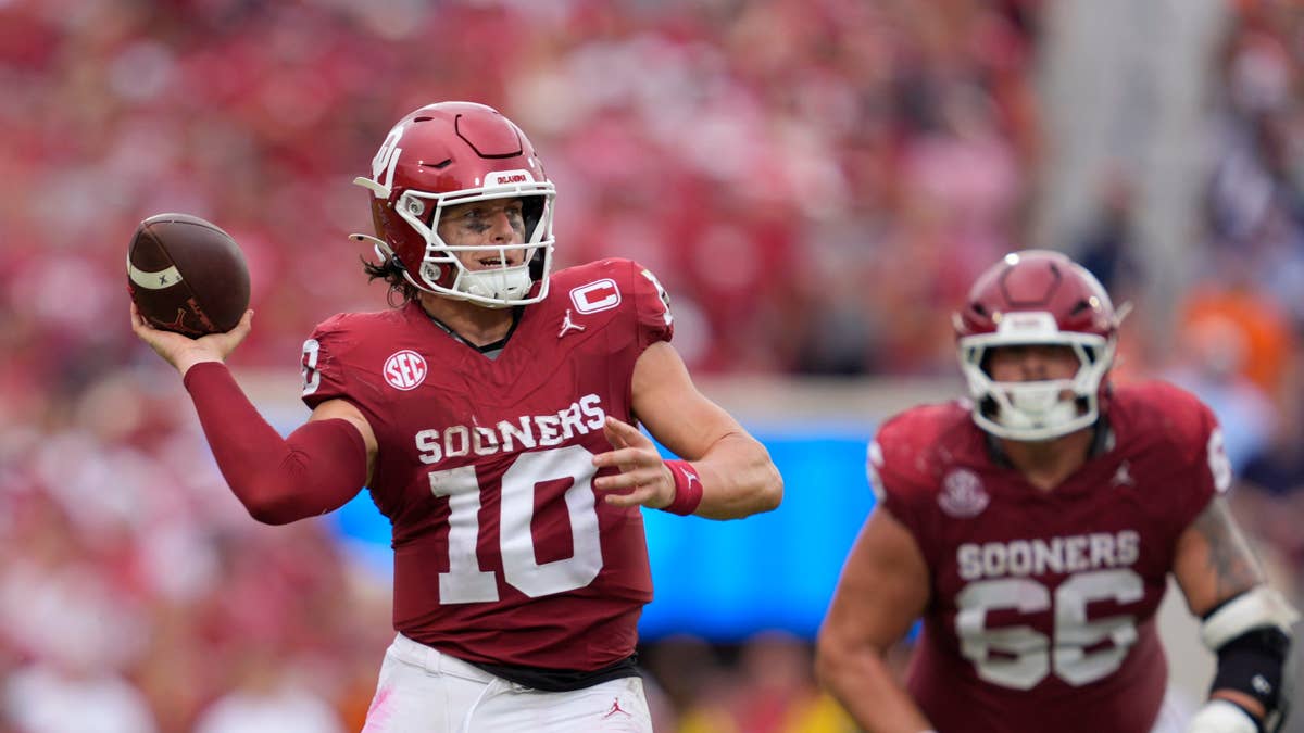 John Mateer #10 of the Oklahoma Sooners throws a pass in a maroon uniform with white numbers.