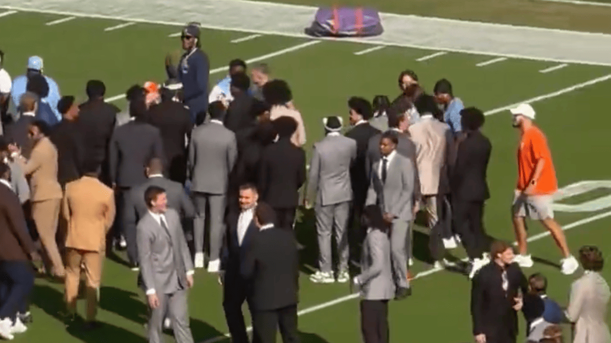 Clemson and UNC players in suits and orange shirts nearly fight on a football field before kickoff.