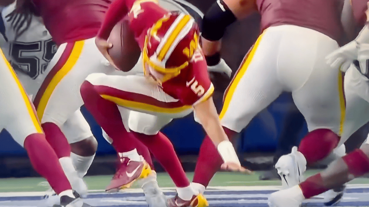 Jayden Daniels in a burgundy and gold Commanders uniform, number 5, is tackled by a player in a white uniform.