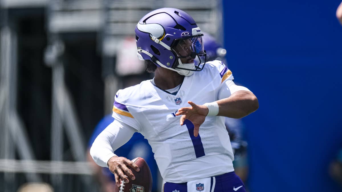 Carson Wentz in a white Vikings jersey with purple and gold trim, number 1, throws a football.
