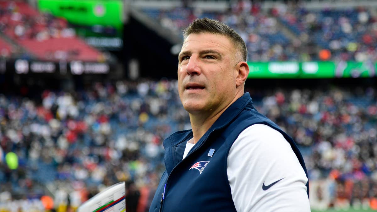 Mike Vrabel in a navy Patriots vest over a white shirt looks on during a game.