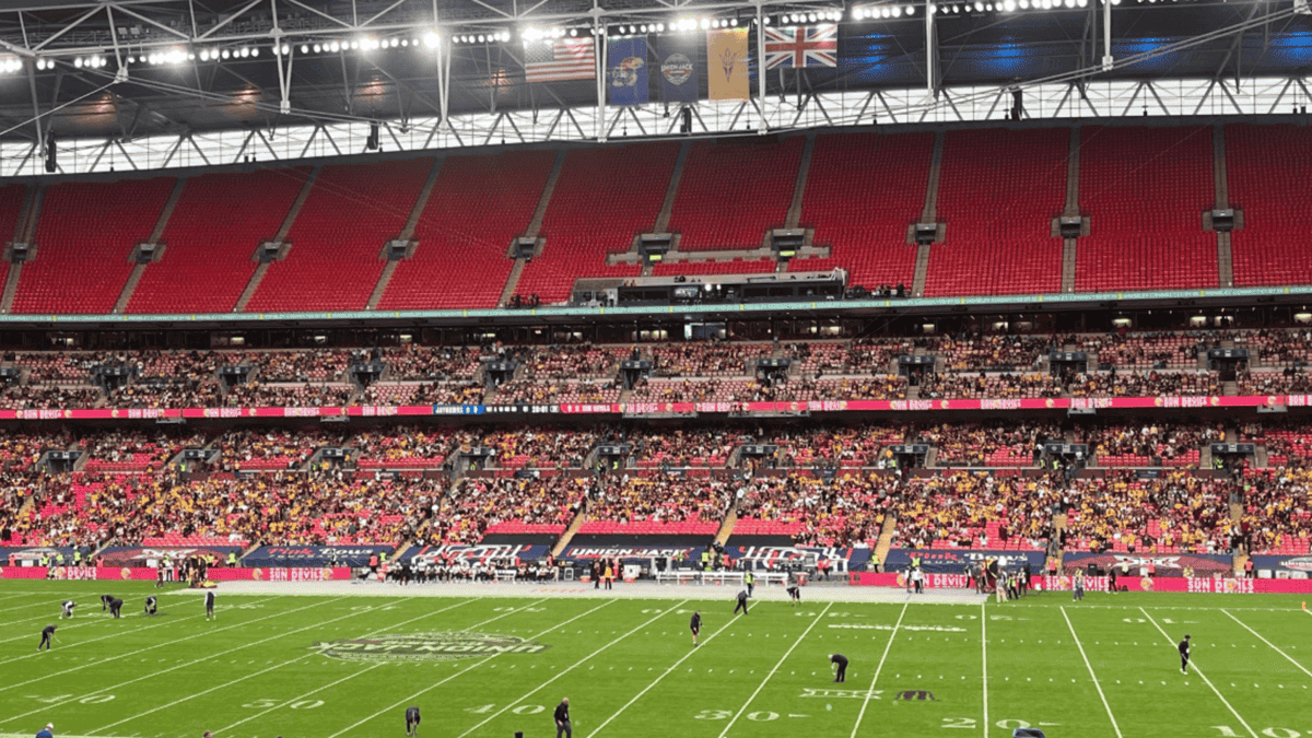 American football field at Wembley Stadium with sparse crowd in red seats and Union Jack banners.