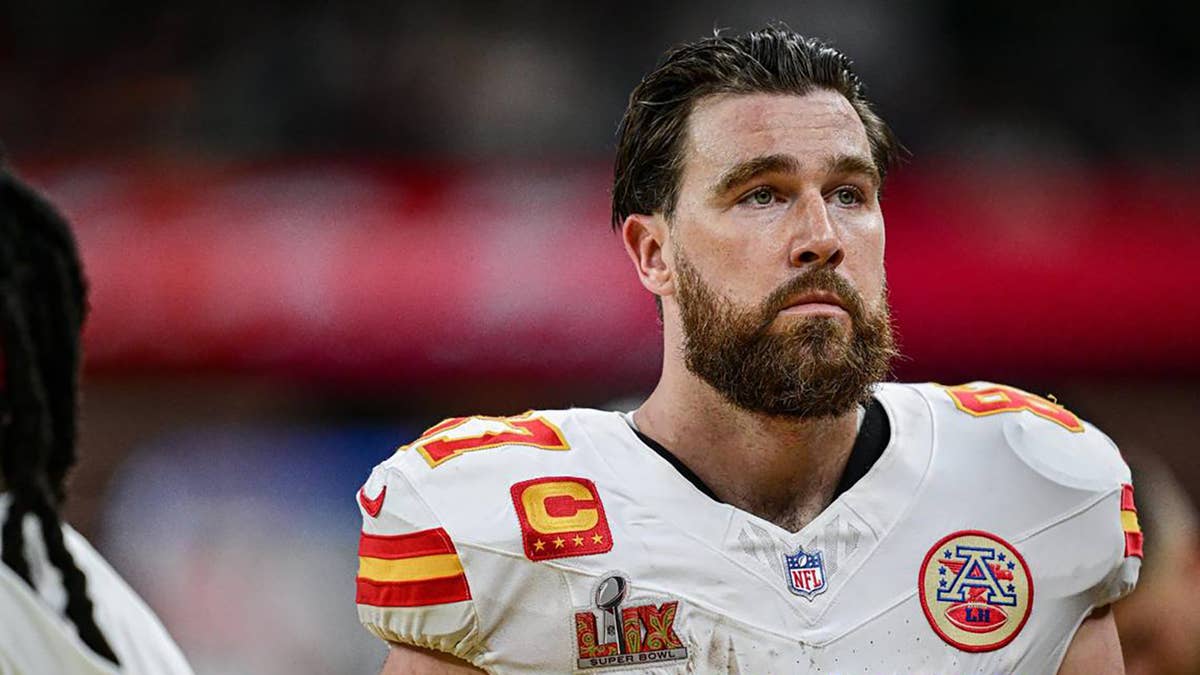 Travis Kelce in a white Kansas City Chiefs jersey with red and yellow stripes and Super Bowl LIX patch.