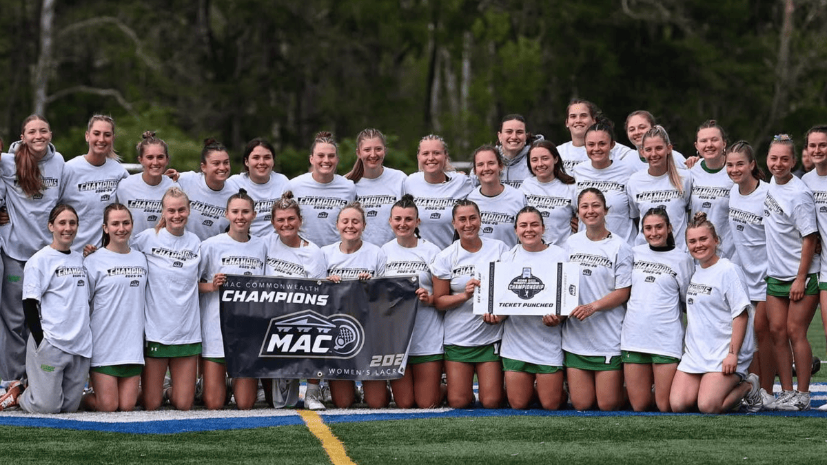 York women's lacrosse team in white "CHAMPIONS" shirts and green skirts hold a MAC Commonwealth Championship banner.